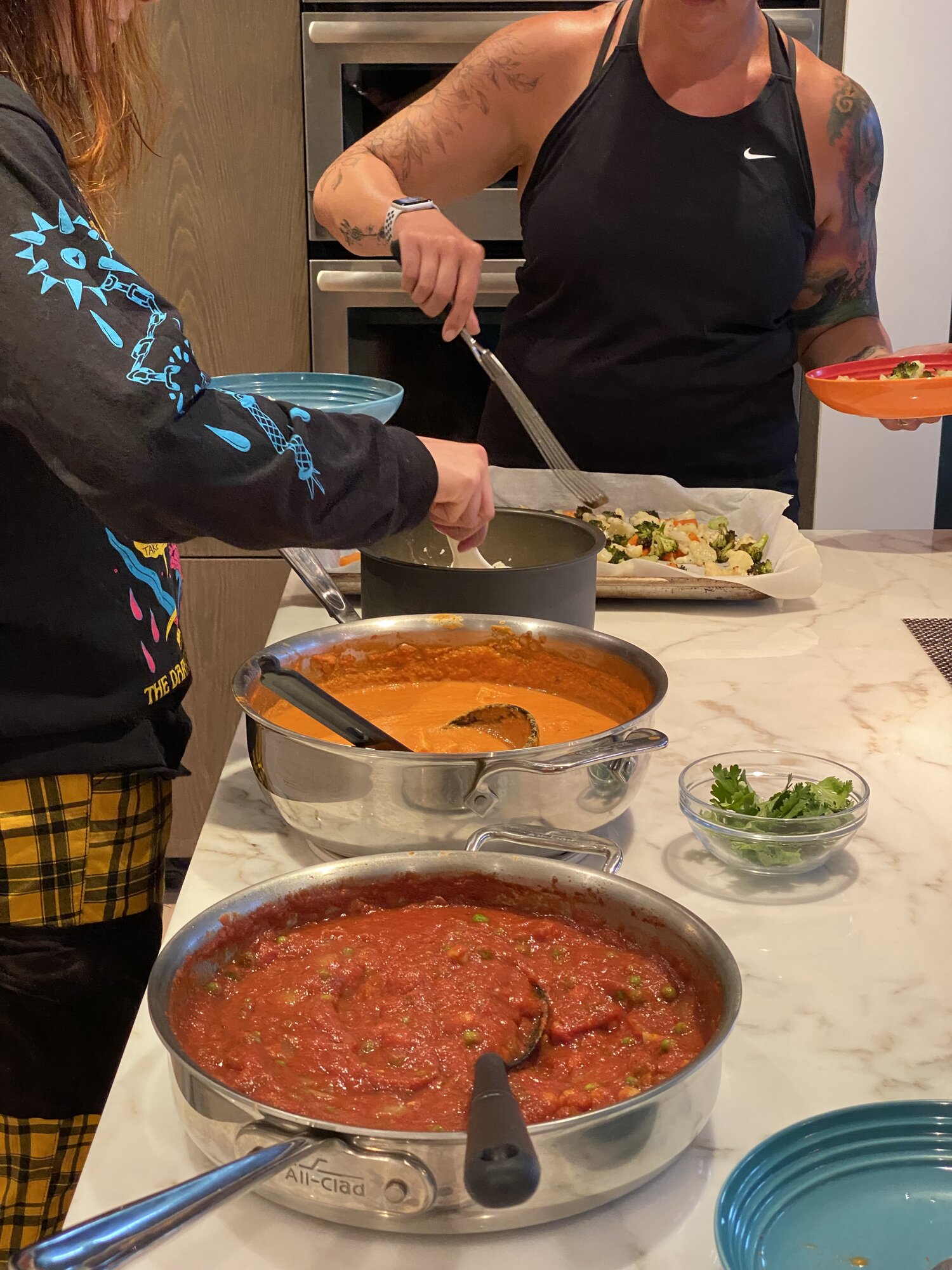 Serving up curry night: a creamy curry, a tomato and pea curry, rice, roasted vegetables, and cilantro on the counter