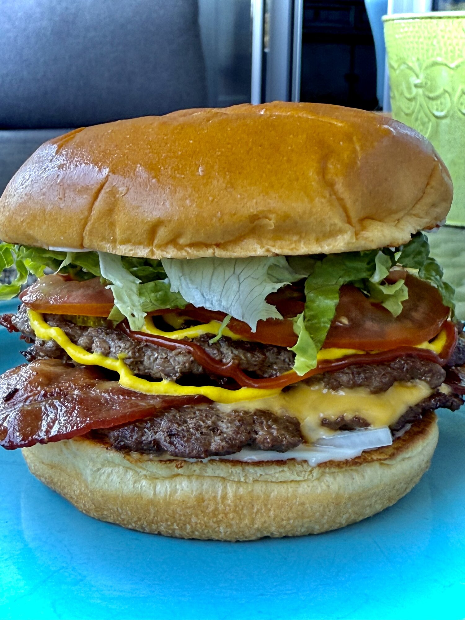 Double bacon cheeseburger with mustard, ketchup, tomato, and shredded lettuce on a brioche bun, on a turquoise plate