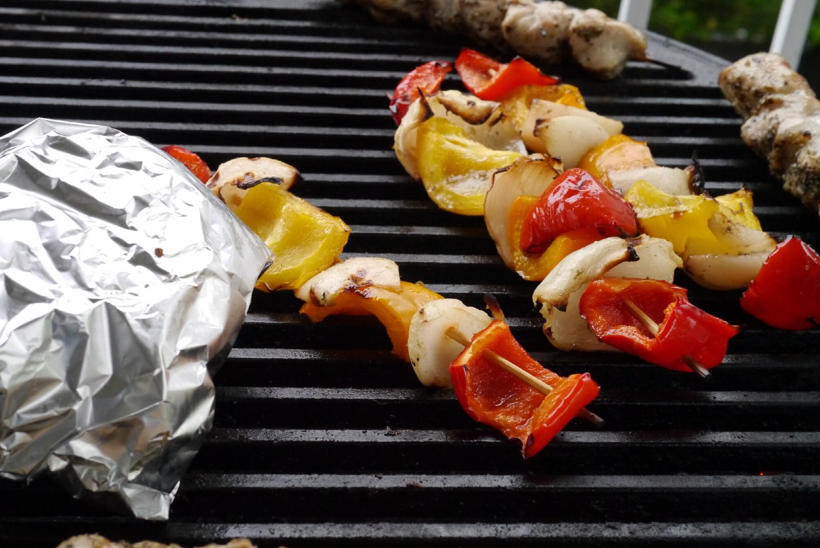 Pepper and onion skewers on a grill next to chicken skewers and a foil packet