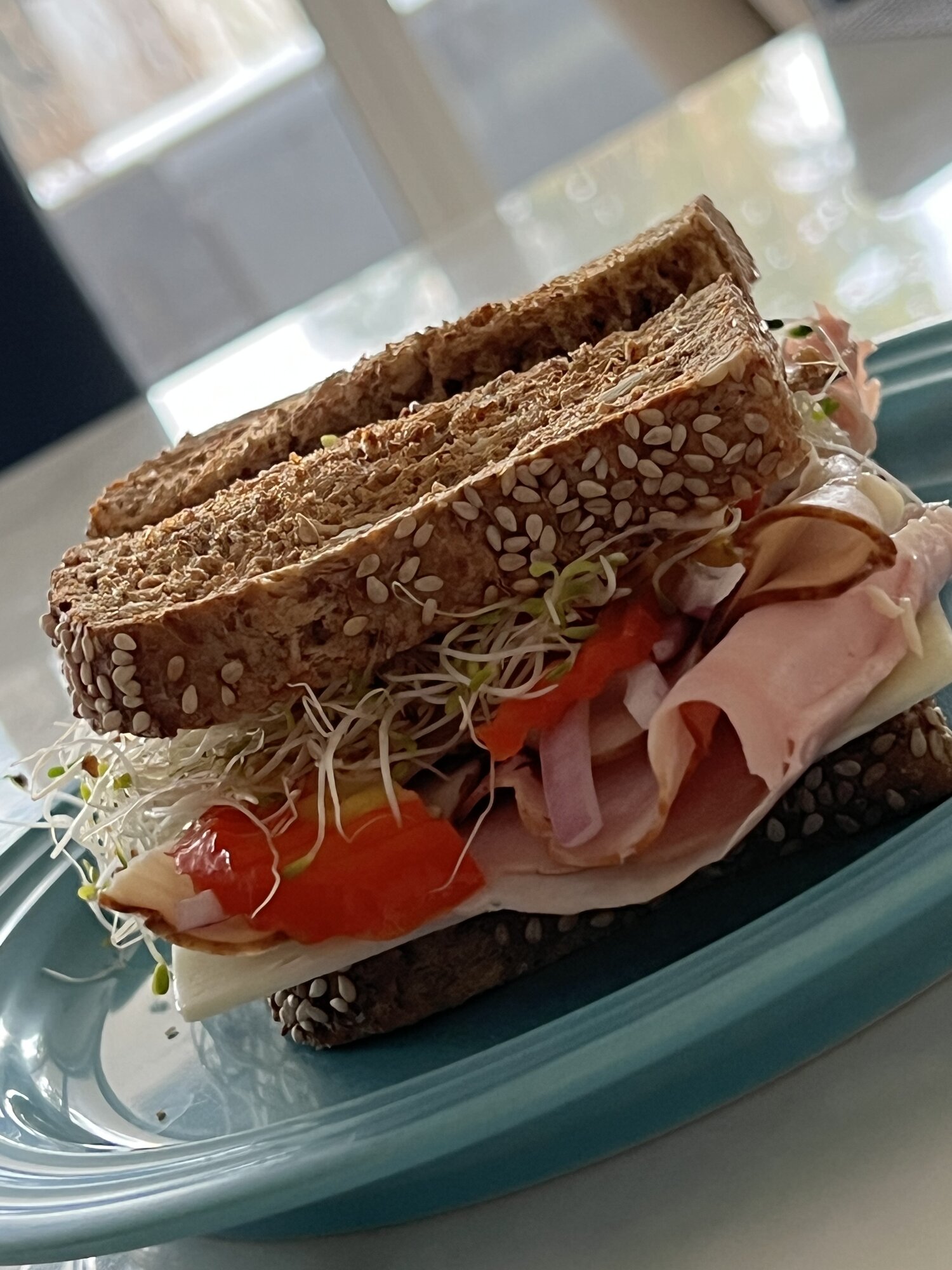 Ham and cheese sandwich on seeded whole grain bread with sprouts, roasted red pepper, and red onion