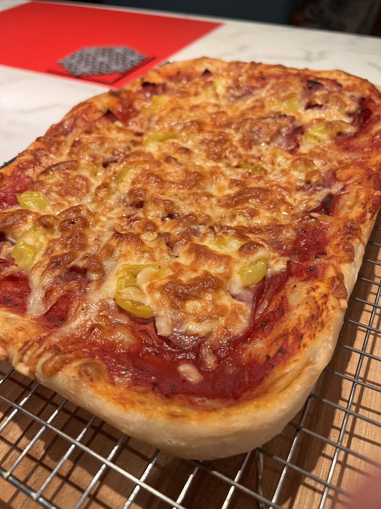 Rectangular pan pizza with ham and banana peppers, cooling on a wire rack