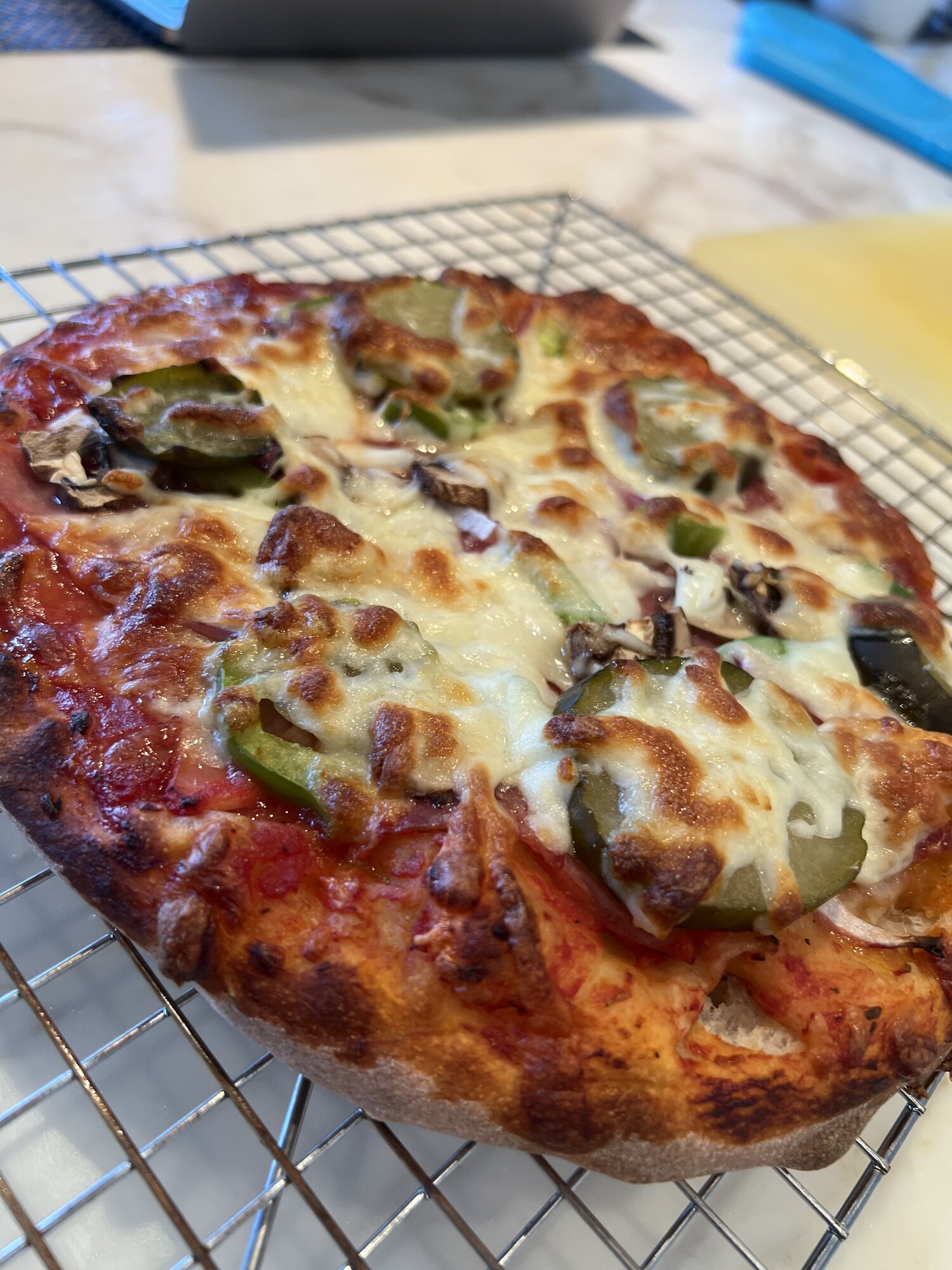Pizza topped with pickles, mushrooms, green pepper, and ham, cooling on a wire rack