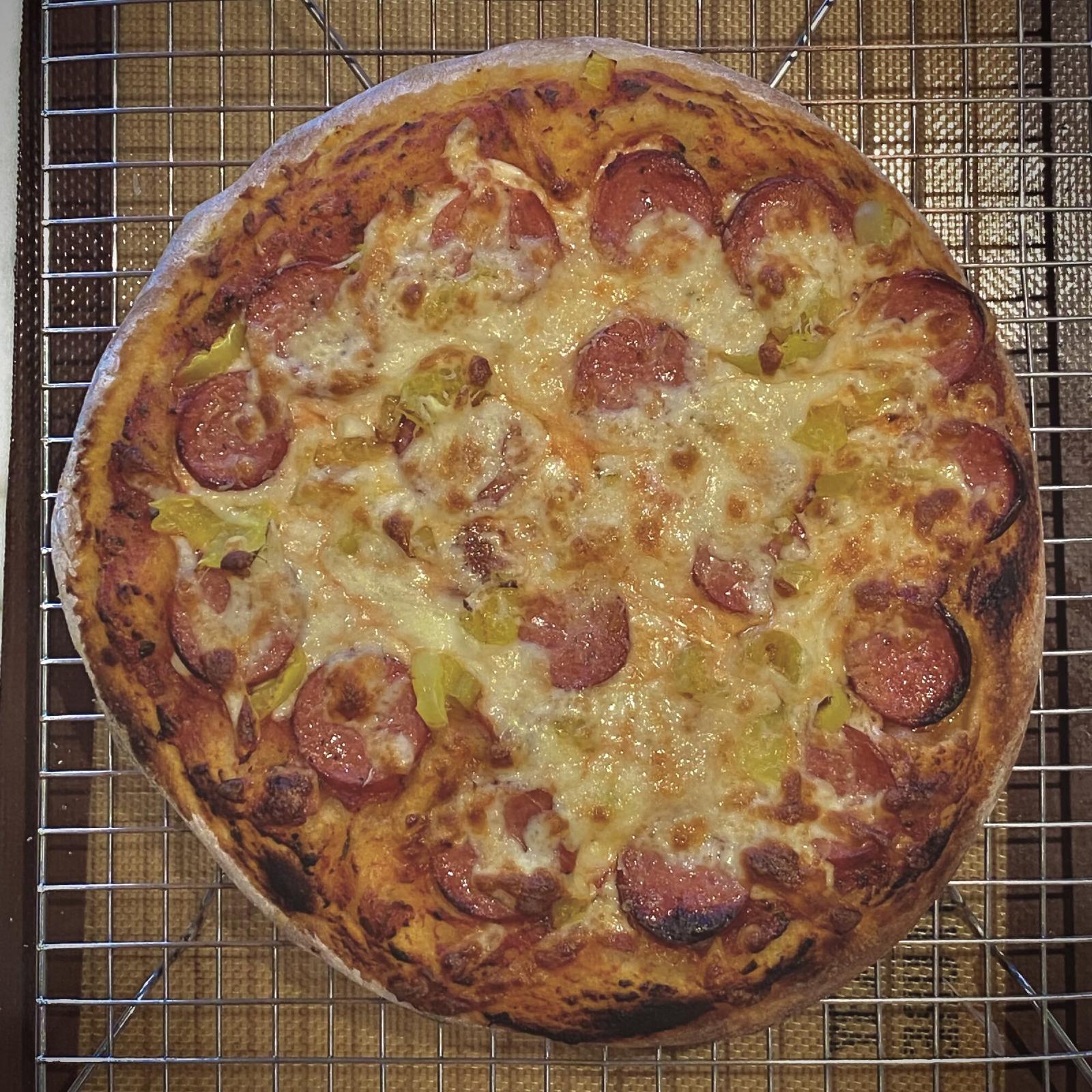 Round pizza with sausage and banana peppers, seen from above on a cooling rack