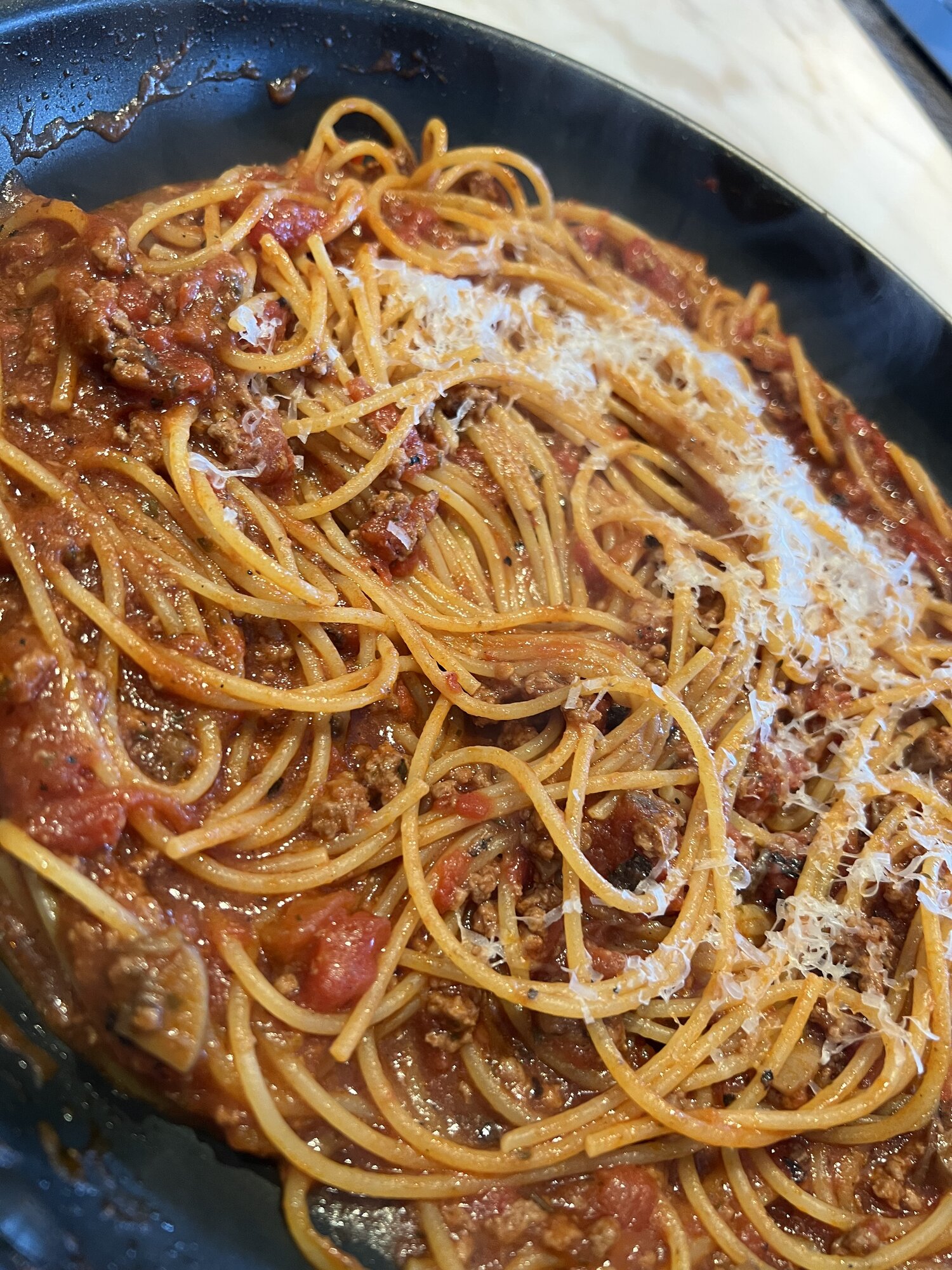 Spaghetti in meat sauce with grated Parmesan, in a dark pan