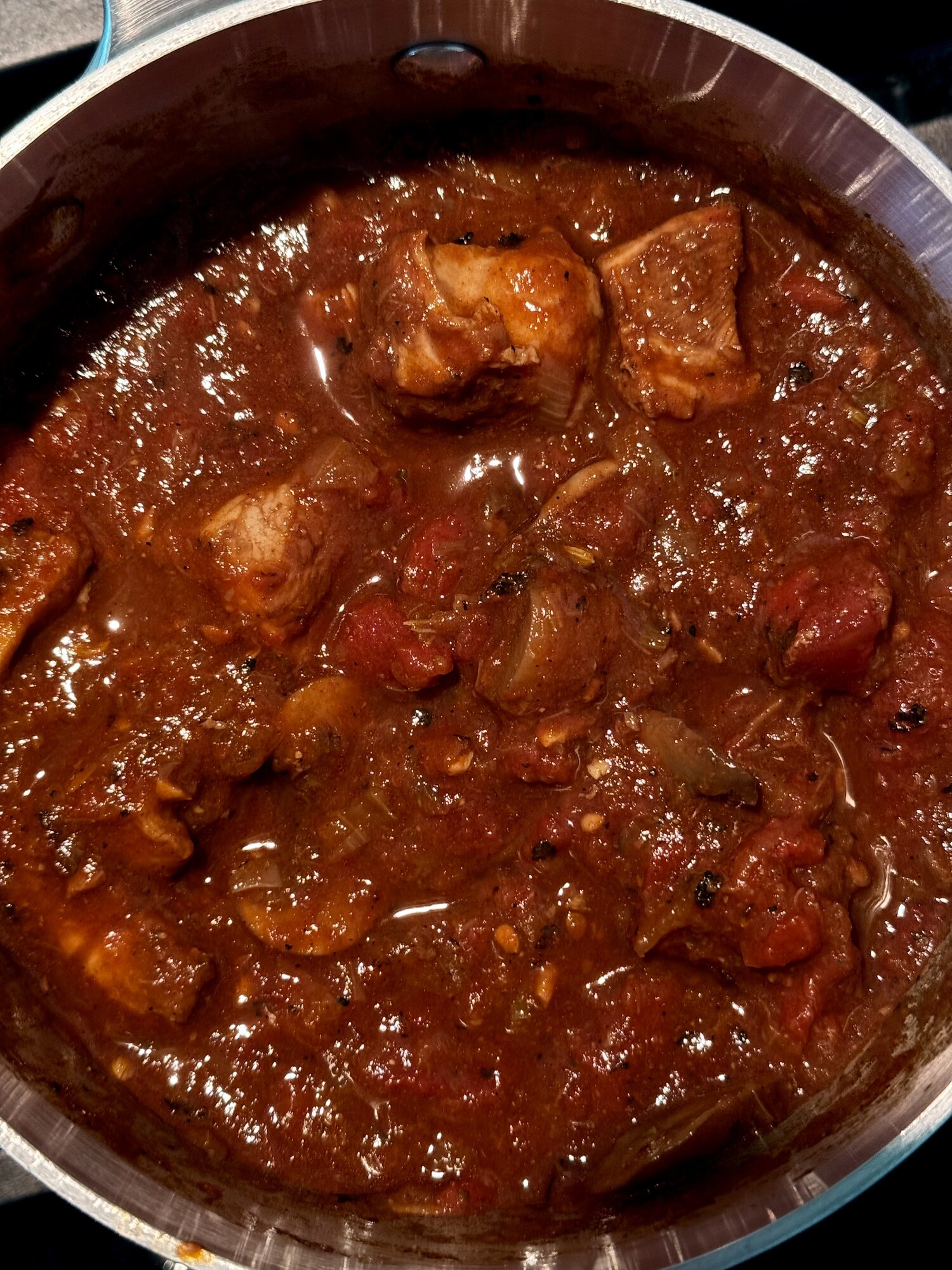 Pork goulash v2 simmering in a stainless pot: oven-browned pork cubes in a thick paprika and tomato sauce with onion and mushroom